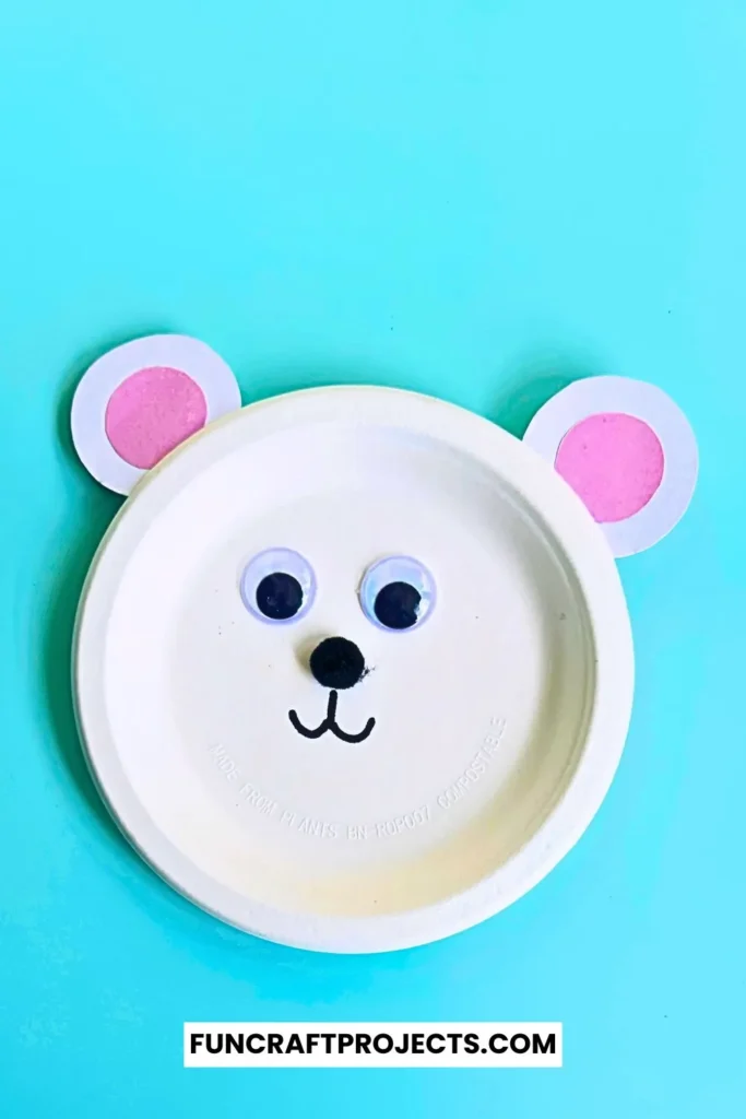 Paper plate polar bear craft with googly eyes, pink ears, and a simple black nose. Easy DIY bear craft for kids, perfect for preschool or winter activities.