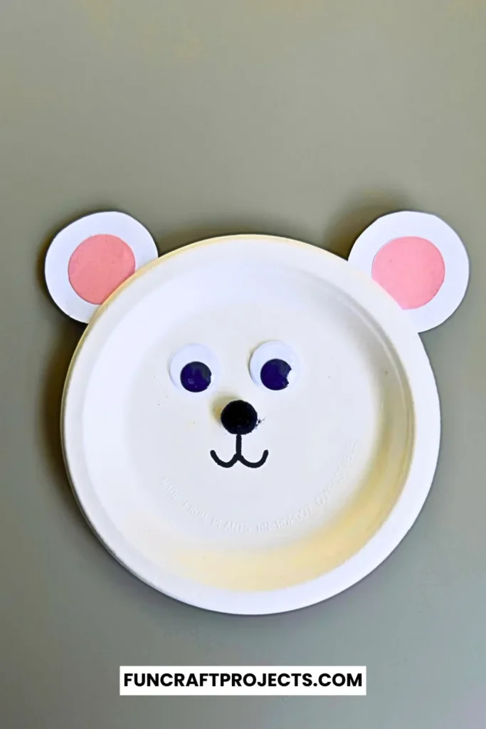 Paper plate polar bear craft with googly eyes, pink ears, and a simple black nose. Easy DIY bear craft for kids, perfect for preschool or winter activities.