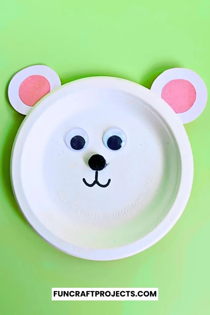 Paper plate polar bear craft with googly eyes, pink ears, and a simple black nose. Easy DIY bear craft for kids, perfect for preschool or winter activities.