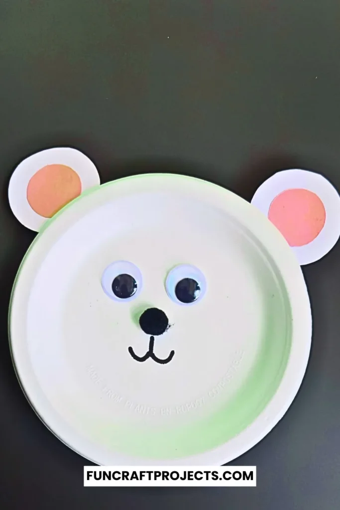 Paper plate polar bear craft with googly eyes, pink ears, and a simple black nose. Easy DIY bear craft for kids, perfect for preschool or winter activities.