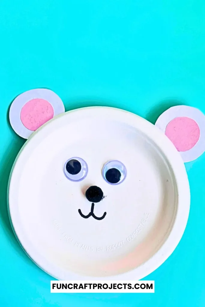 Paper plate polar bear craft with googly eyes, pink ears, and a simple black nose. Easy DIY bear craft for kids, perfect for preschool or winter activities.