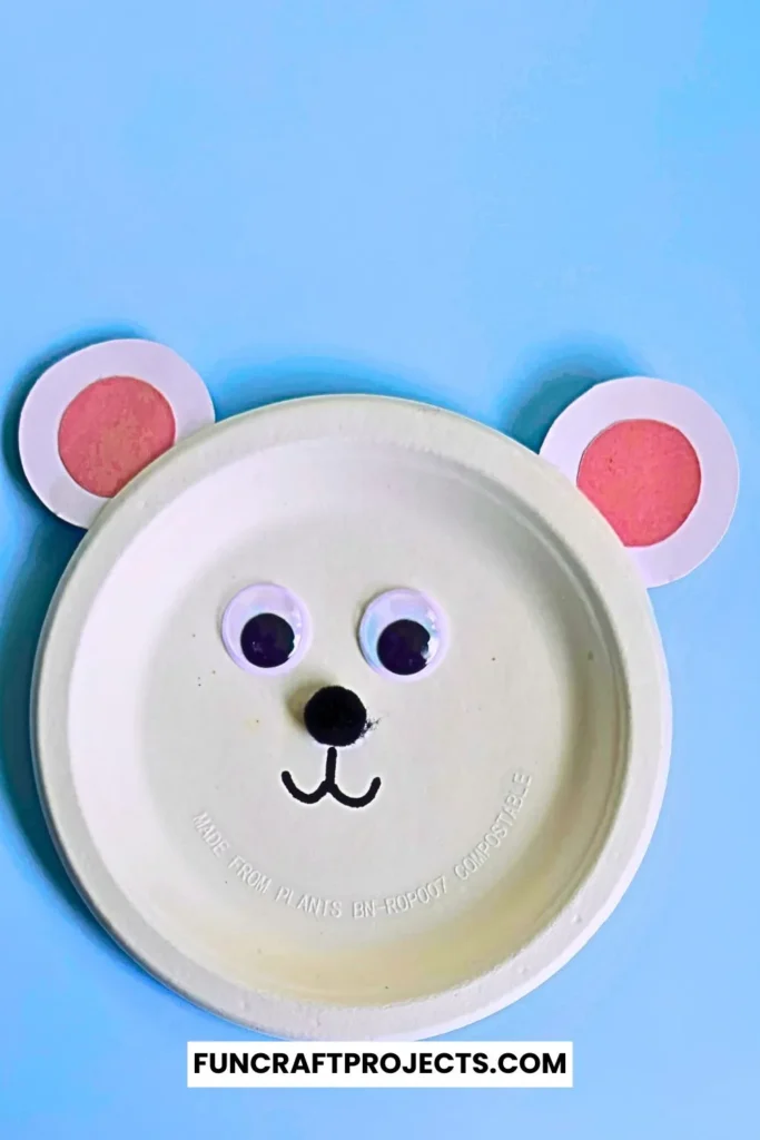 Paper plate polar bear craft with googly eyes, pink ears, and a simple black nose. Easy DIY bear craft for kids, perfect for preschool or winter activities.