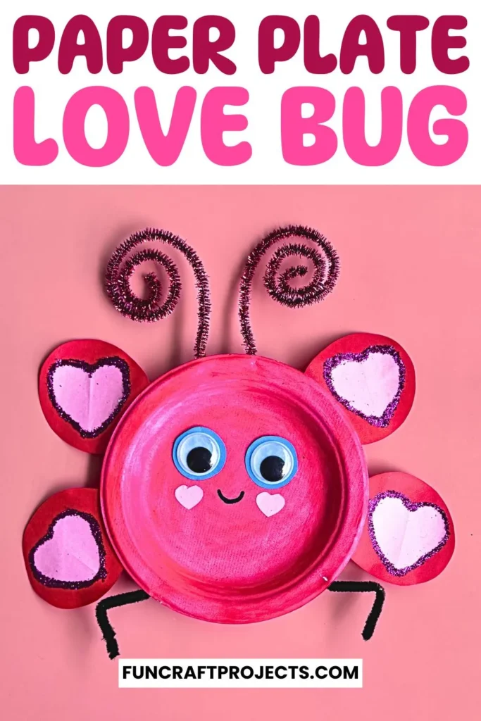 Paper plate love bug craft with pink paint, heart-shaped wings, googly eyes, and pipe cleaner antennae on a beige background.