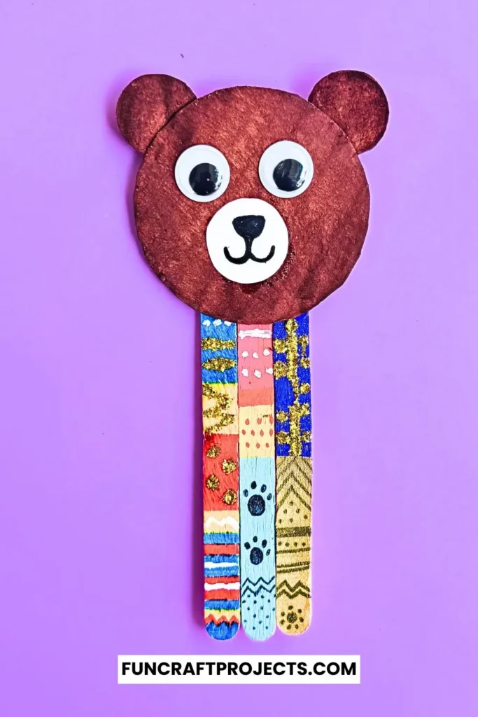 Handmade popsicle stick teddy bear bookmark craft with colorful patterns and googly eyes, crafted from jumbo popsicle sticks and brown craft paper