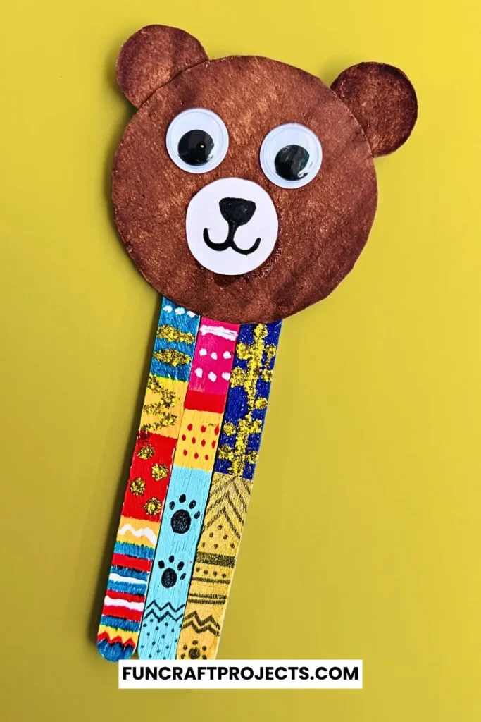 Handmade popsicle stick teddy bear bookmark craft with colorful patterns and googly eyes, crafted from jumbo popsicle sticks and brown craft paper