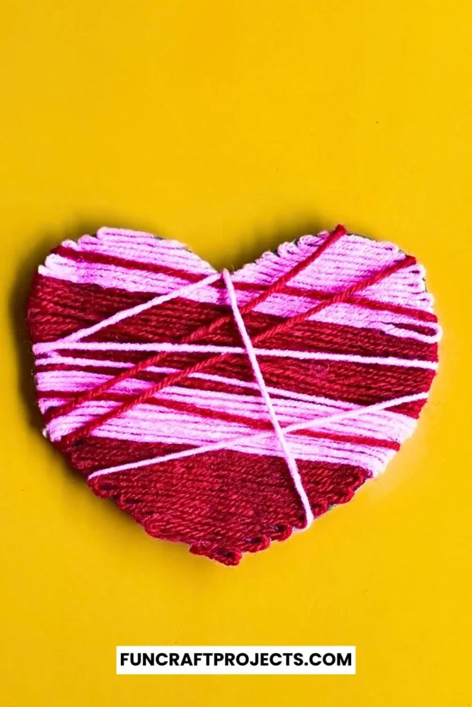 A vibrant yarn wrapped heart craft featuring pink and red yarn, wrapped intricately around a sturdy heart-shaped cardboard, perfect for Valentine’s Day.