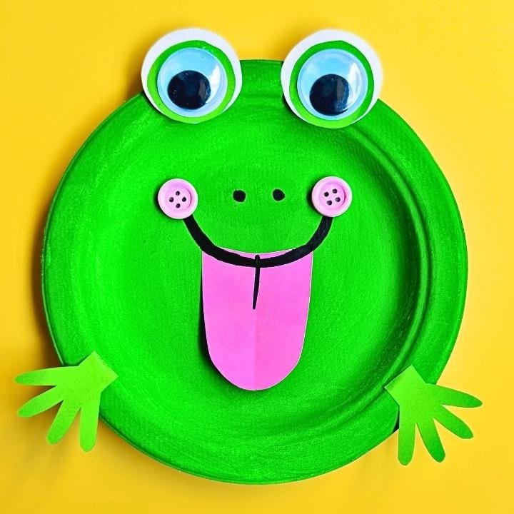 Paper Plate Frog Craft – A bright green paper plate frog with big googly eyes, a pink tongue, and cut-out hands, perfect for preschool crafts and fun activities